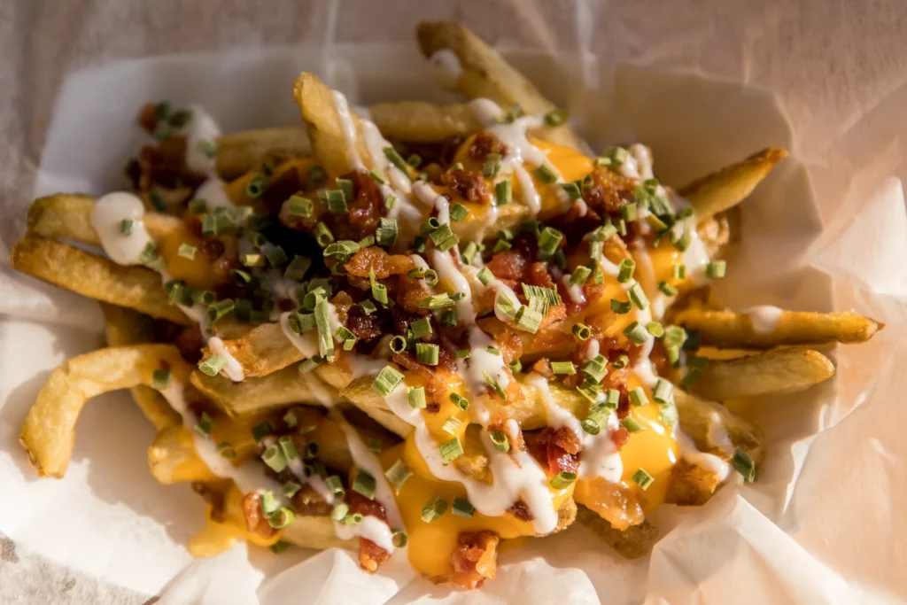 Loaded fries with cheese sauce, creamy toppings, and savory garnish in a paper-lined container