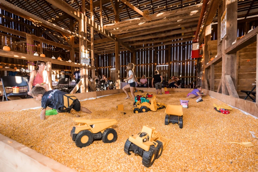 Rustic barn corn pit with children playing and toy trucks inside a farm attraction.